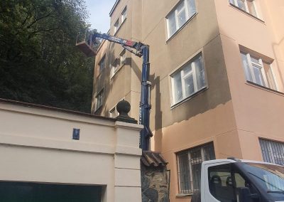 Průběh aplikace fasádního nátěru staršího bytového domu v Praze 5 z hydraulické plošiny