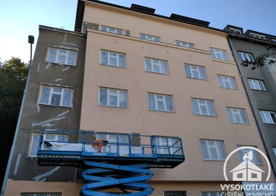Průběh aplikace nového nátěru fasády staršího bytového domu v Praze 5 z hydraulické plošiny